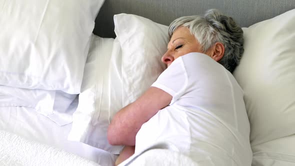 Senior woman sleeping on bed in bedroom alt