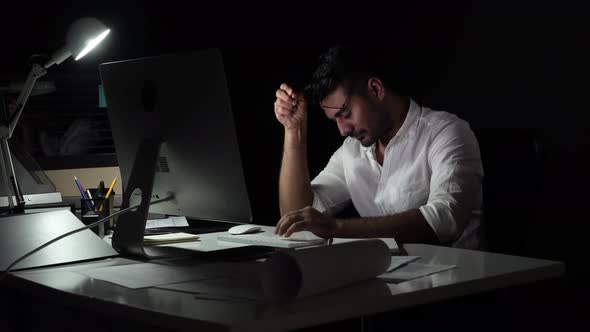 Fatigued sleepy workaholic Asian man yawning while working late at night in dark office