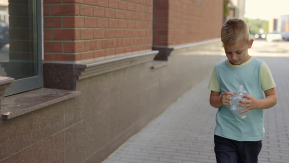School Boy is Holding the Plastic Bottle and Puts It to the Correct Bin Fot Plastic alt