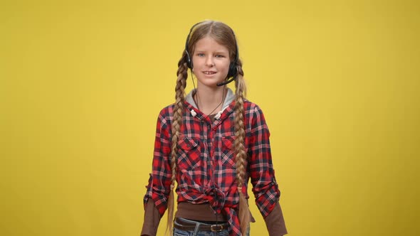 Positive Caucasian Teenage Girl in Headphones with Microphone Talking Gesturing at Yellow Background alt