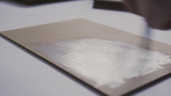 An Artist Primes Canvas with White Paint on Paper at a Drawing School