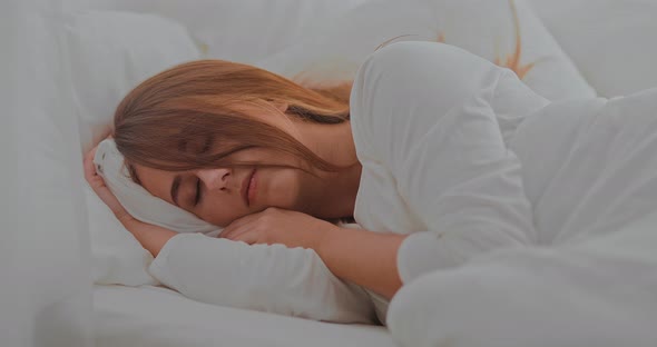Beautiful Girl Sleeps Soundly in Bed Under a White Blanket