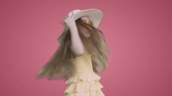 Child Girl in Yellow Dress and Hat is Dancing Ang Singing on Pink Background alt