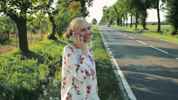 Young Lady Speaking on Phone While Hitchhiking. alt