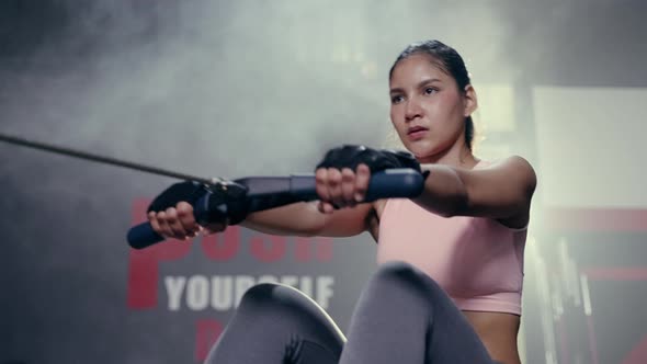 asian Female exercising in fitness club. Fitness young asian woman using rowing machine in the gym