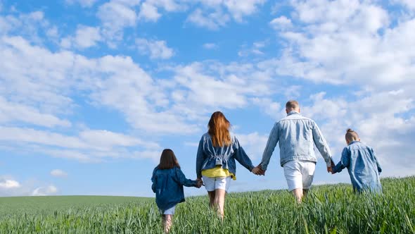 Happy Family Holding Hands Walking on a Green Field alt
