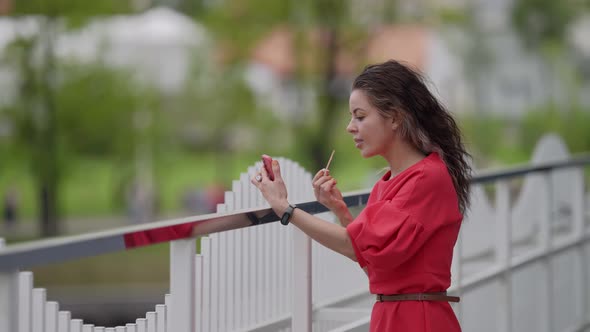 Young Pretty Woman is Applying Lip Balm on Street Correcting Makeup During Walk in City alt