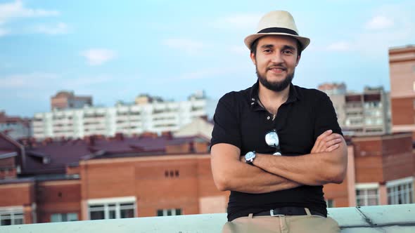 Portrait of Happy Caucasian Man in Hat with Arms Crossed Outdoor on Roof or Balcony alt