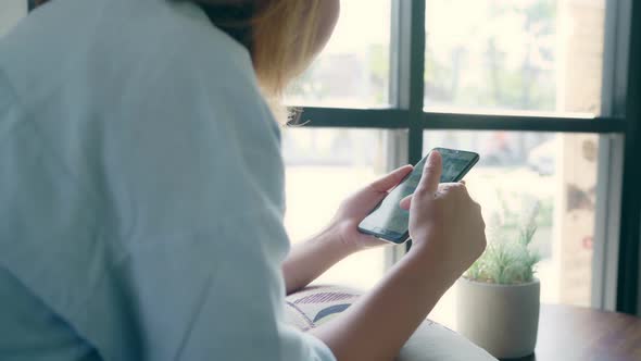 Asian woman using smartphone for talking, reading and texting while sitting on table in cafe.