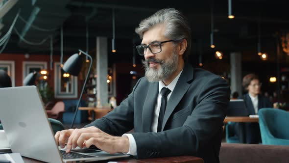 Mature Entrepreneur Using Laptop Computer in Restaurant Typing at Table Alone alt
