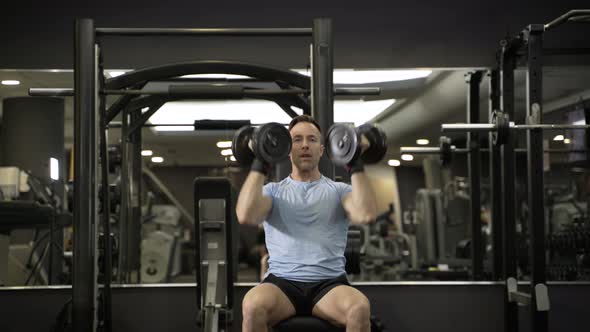 Muscular man holding dumbbell above the head at the gym. alt