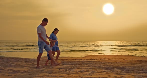 Happy Family Walks Along the Seashore at Sunset Parents Hold Their Son's Hands