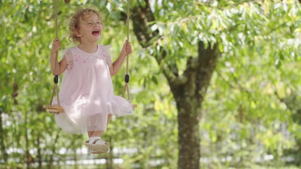 Spring and happy summer time. Joyful smiling little girl swinging on the swing, child with blue eyes