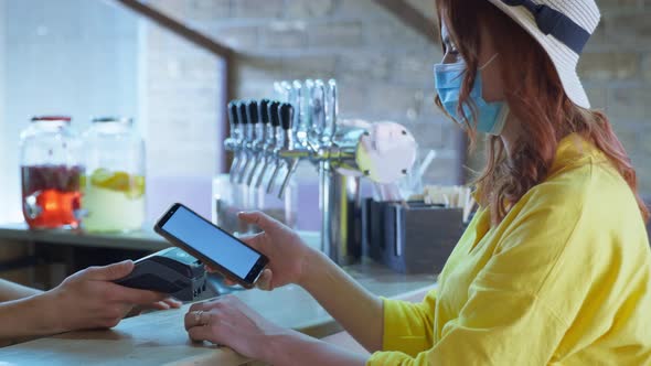 Cafe Employees Calculates a Buyer in a Medical Mask Using a Contactless Mobile Phone in a Credit alt