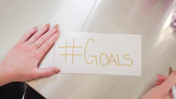 Female Hands Writing Hashtag Goals On A White Piece Of Paper