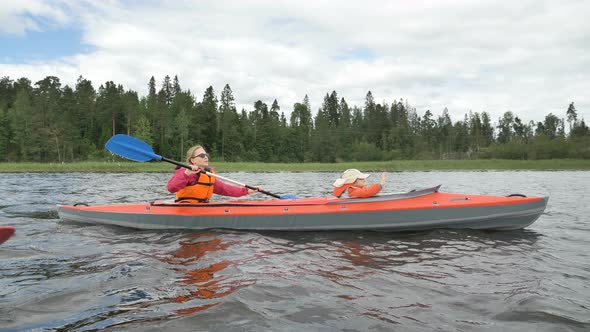 Lady in Glasses Rows Kayak with Daughter Sailing Along Lake alt