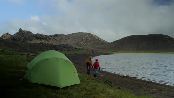 beautiful iceland landscape, two hikers walking together by the lake with a tent pitched in a foregr