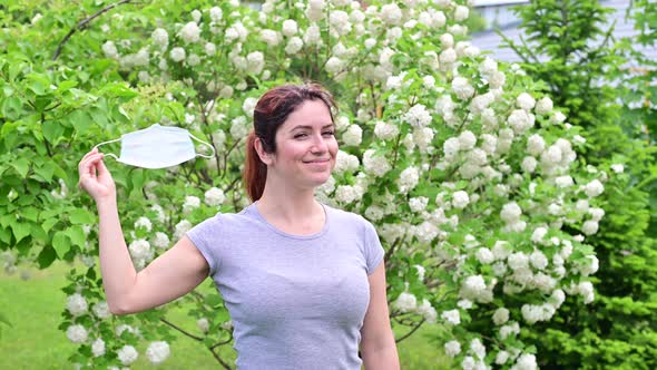 A Woman in a Gray Tshirt Happily Takes Off Her Medical Mask at the End of Quarantine alt