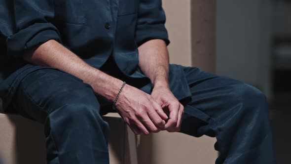 Man in Prison Clothes Sits on Boxes and Nervously Picks His Fingers
