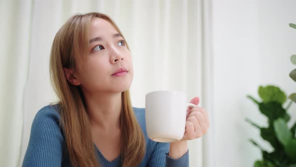 Beautiful young Asian woman drinking a hot coffee enjoyed looking out window