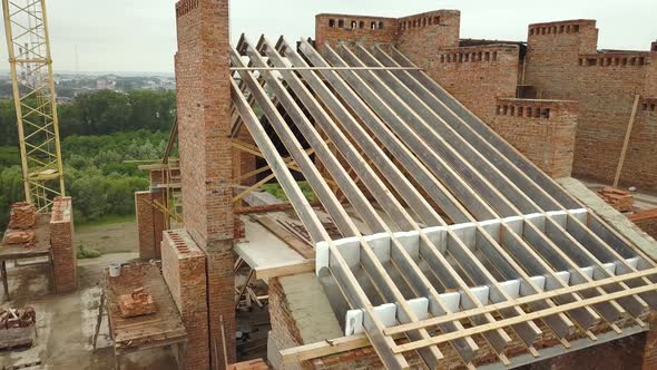 Aerial view of unfinished brick apartment building with wooden roof structure under construction. alt
