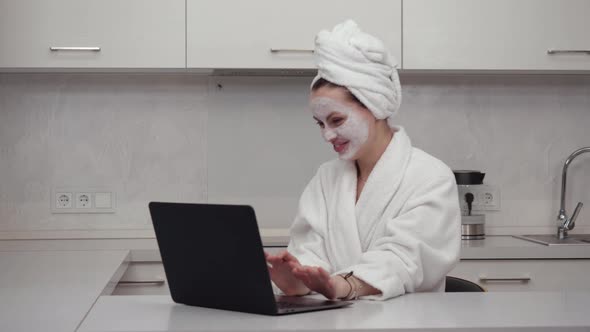 Young Girl in a Robe Face Mask Cheerfully Talking on the Web Camera Laptop