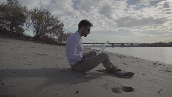 Man Working On Laptop And Sitting On Beach. Creative Man With Computer Overtime Working Outdoor. alt