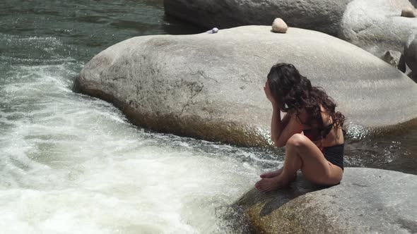 Curly haired lady in bikini washes face with river water