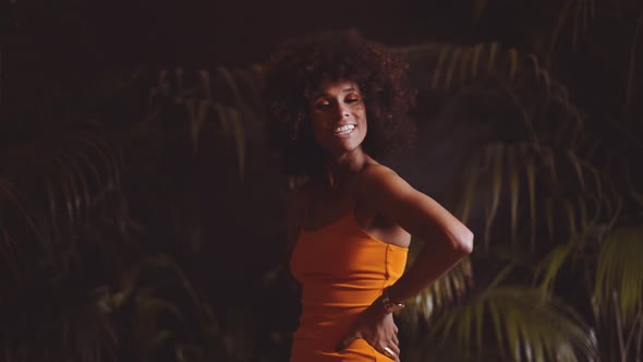 Model With Afro Smiling Then Posing With Attitude To Camera In Orange Dress alt