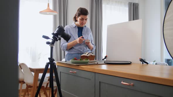 Food Blogger with Camera Icing Cake in Kitchen