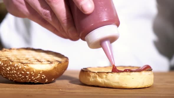 chef squeezes tomato sauce crisp toasted bun wooden table in restaurant kitchen