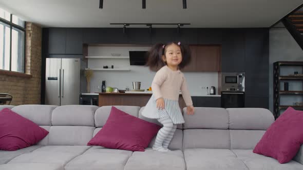 Excited Cute Asian Toddler Girl Jumping on Sofa alt