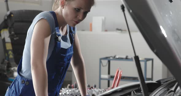 Professional female mechanic doing a car service, she is checking a car engine