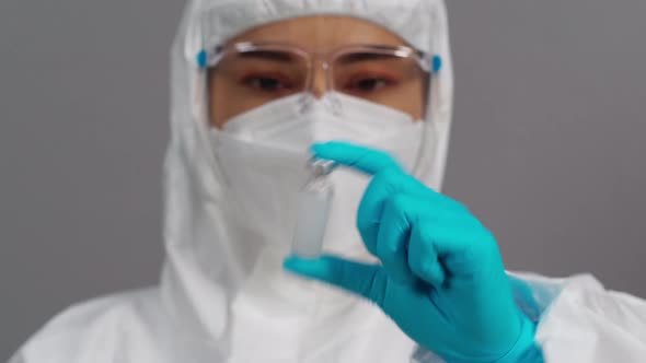 doctor in protective PPE suit holding and gently shaking vaccine bottle