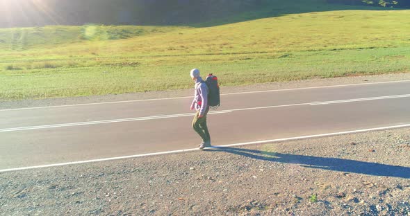 Flight Over Hitchhiker Tourist Walking on Asphalt Road, Huge Rural Valley at Summer Day alt