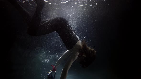 A Woman in a Suit Is Swimming Underwater Doing a Somersault in the Water Her Long Hair Flying alt