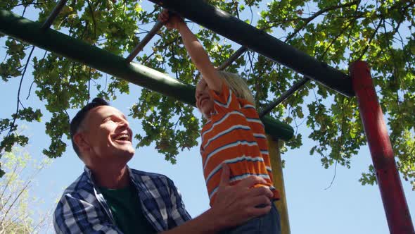 Father assisting son on climbing monkey bars at playground 4k alt