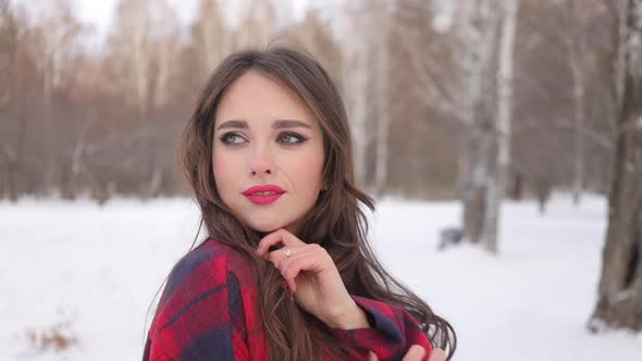 Young Woman with Wavy Hair Standing and Touching Face in Winter Forest