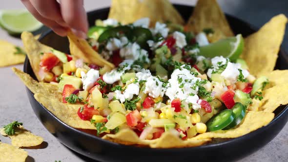 Mexican street corn salad with cheese and nachos chips in black plate. 