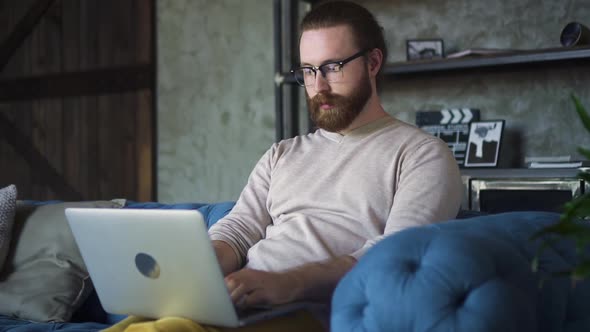 Young Bearded Businessman is Working on Online Project and Using Laptop at Apartment Spbd alt