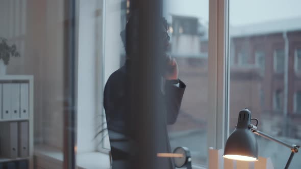 Businessman Speaking on Cell Phone near the Window in Modern Office alt