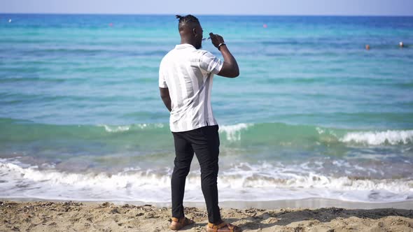 Back View Wide Shot of Handsome African American Bearded Man Standing on Sandy Beach Putting on alt