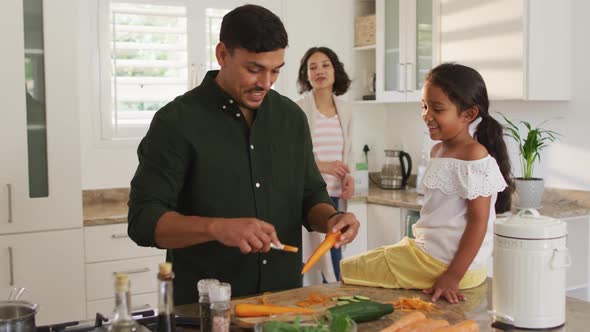Hispanic father teaching daughter sitting on countertop cooking alt