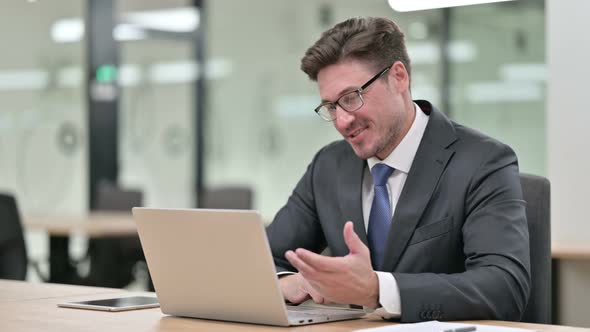 Cheerful Middle Aged Businessman Talking on Video Chat on Laptop in Office  alt