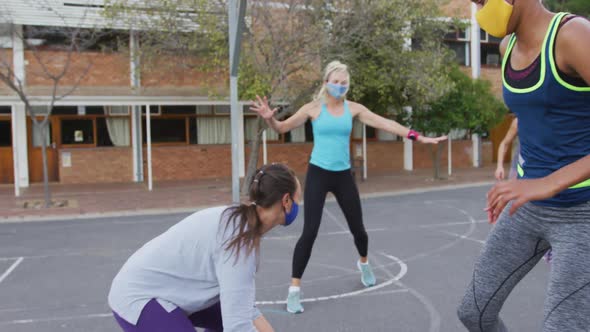 Diverse female basketball team wearing face masks playing match, scoring goal alt