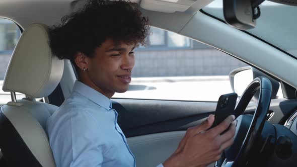 Young Business Guy of Ethnicity Scrolls the News Feed on the Smartphone While Sitting in the Car alt