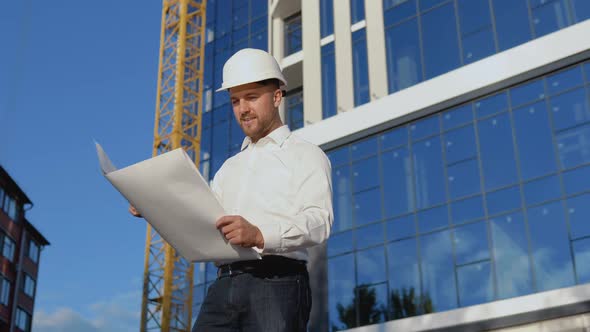 An Engineer in a White Shirt and Helmet Works on the Construction of a Modern Glass Building alt