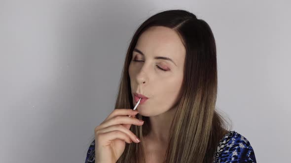 An attractive woman with long brown hair looking sexy and seductive while sucking a lolly pop