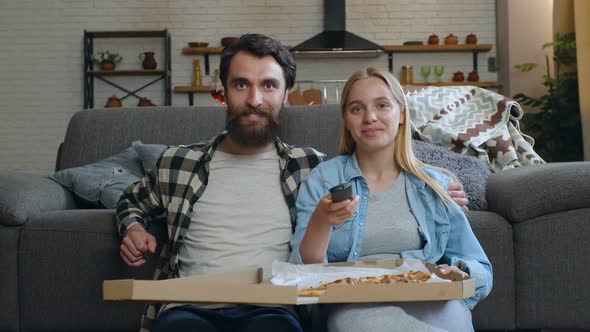 Couple eating pizza and watching TV at home. 