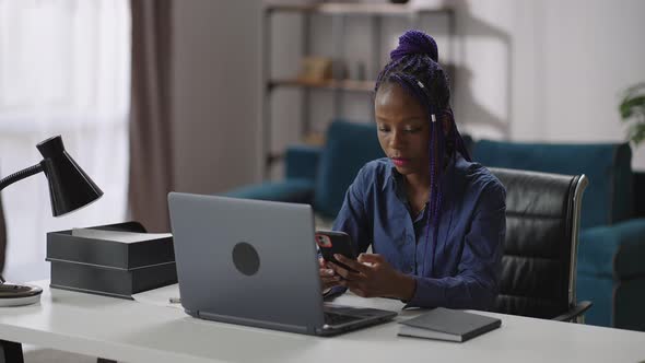 Young Afroamerican Businesswoman is Using Smartphone in Working Place in Her Office Sitting at Table alt